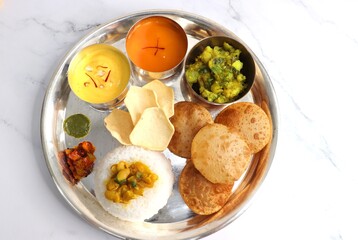 Indian vegetarian Thali or platter includes Aloo ki sabji, dal rice, Puri bhaji, Shrikhand or Srikhand, Aamras, papad, pickle, and chutney. Indian food is served in a Silverplate or thali. Copy Space.
