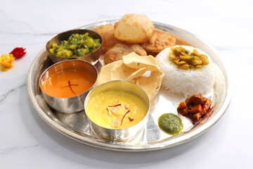 Indian vegetarian Thali or platter includes Aloo ki sabji, dal rice, Puri bhaji, Shrikhand or Srikhand, Aamras, papad, pickle, and chutney. Indian food is served in a Silverplate or thali. Copy Space.