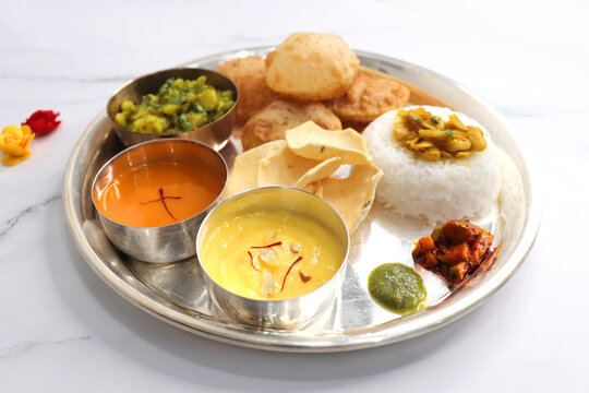 Indian vegetarian Thali or platter includes Aloo ki sabji, dal rice, Puri bhaji, Shrikhand or Srikhand, Aamras, papad, pickle, and chutney. Indian food is served in a Silverplate or thali. Copy Space.