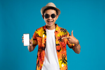 Handsome man in beach shirt pointing at his cellphone which he is holding on a blue background