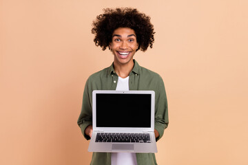 Portrait of attractive cheerful amazed trendy wavy-haired guy holding laptop copy space isolated over beige pastel color background