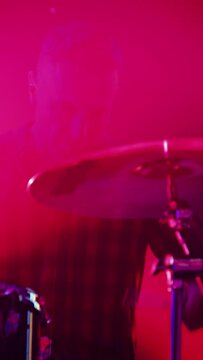 Vertical Footage of a Rock Band Performing at a Concert in a Night Club. Close Up Portrait of a Drummer Playing the Drums. Live Music Party in Front of Bright Colorful Lights on Stage.