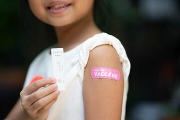 Asian little girl showing plaster with COVID-19 rapid test kit - home ag test kit COVID-19 rapid antigen test, herd immunity, side effect, booster dose, vaccine passport and Coronavirus pandemic