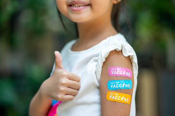 Asian young girl showing her arm with multicolored bandage after got vaccinated or inoculation,...