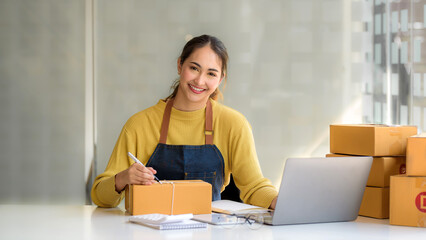 Young Asian small business owner woman hold pen and parcel boxes to write down addresses for delivery to their customers' homes. Looking at camera.