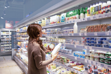 Mature woman chooses dairy products at supermarket.Wide choice of fresh and organic products - obrazy, fototapety, plakaty