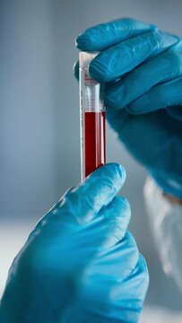 Covid-19 Test Analysis: Scientist Wearing Coverall and Surgical Gloves Holds Blood Test Tube Marked Covid-19. Close-up Camera Shot