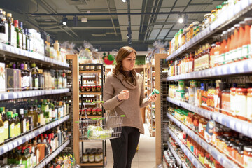 Mature woman chooses groceries . Wide choice of organic preserved products