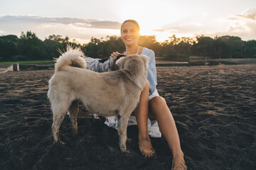 Portrait of joyful woman having fun with adorable mongrel dogs spending leisure at seashore sandy...