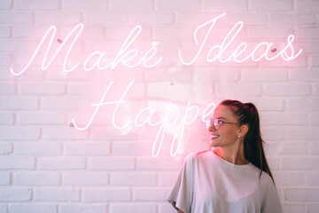 Happy Caucaisan hipster girl in trendy spectacles smiling near icon slogan with inspirational and...