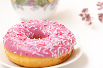 Pink Donut with colorful sprinkles, a floral cup and floral decor on white background, spring snack concept.