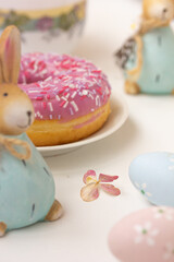 Easter decoration, pink donut with colorful sprinkles, and Easter rabbits, colored eggs, cup on white background