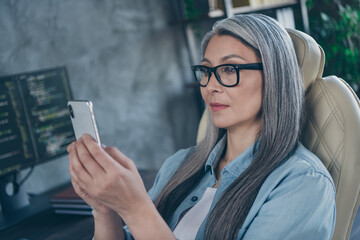 Portrait of attractive smart clever focused grey-haired woman coder using device gadget app at work...