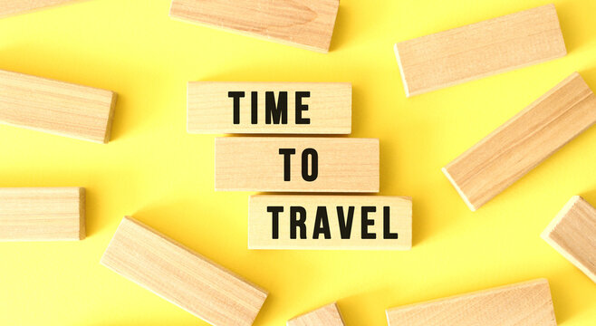 The words TIME TO TRAVEL are written on scattered wooden blocks on a yellow background.