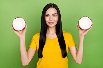 Portrait of gorgeous satisfied person hold two half coconut isolated on green color background