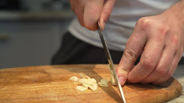 Chef slicing garlic cloves on the cutting board with a knife