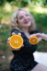 portrait of a charming blonde teenage girl with a fresh orange outdoors in forest or park. tasty juicy fruit