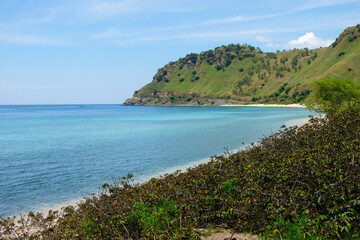 Fototapeta na wymiar The stunning turquoise ocean and crystal clear water of Cristo Rei Back Beach surrounded by green hills during wet season in capital Dili, Timor Leste