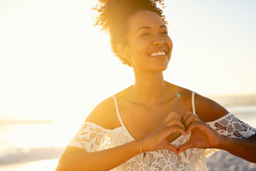 African beautiful girl making hand heart at beach during sunset