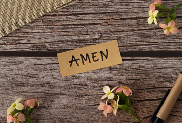 Amen, handwritten text with uppercase letters in English on a wooden table with flowers and pen in vintage style. Top view, flat lay. - obrazy, fototapety, plakaty
