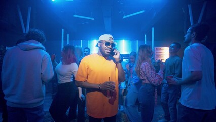 An African-American man talking on the phone in a nightclub on the dance floor under the light of colored spotlights. Night club