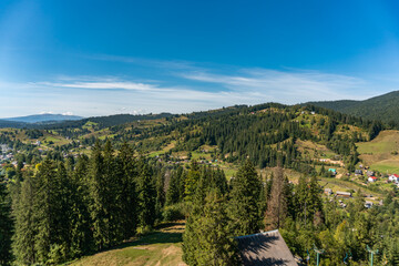 Fototapeta na wymiar Aerial view on the hills, mountains, green forest and houses in a small village on a bright sunny day