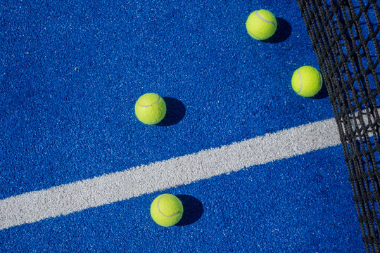 selective focus four paddle tennis balls on a blue paddle tennis court with a net in the background