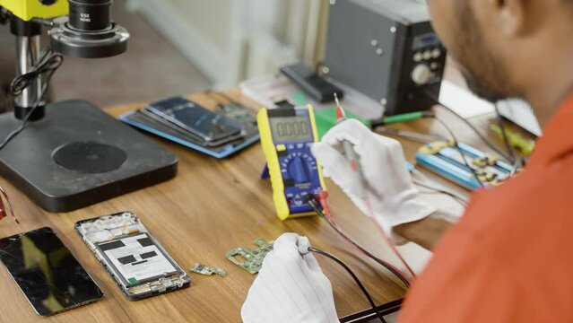 Shoulder shot of repariman busy checking mobile phone circuit board at repair service center - concept of professional occupation, skilled jobs, technician.
