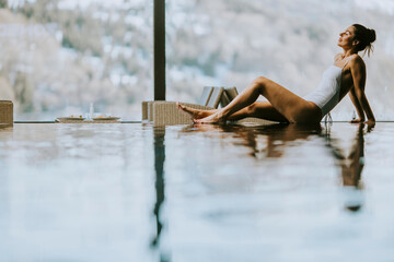 Young woman relaxing on the poolside of infinity swimming pool at winter time