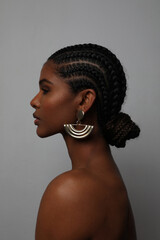 Close-up of African young woman with braids and earrings posing on grey wall. - obrazy, fototapety, plakaty