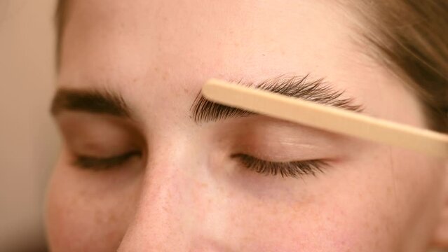 Permanent eyebrow styling. The master applies the composition for laminating the eyebrows with a wooden spatula. 