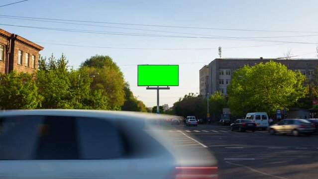 4K Time Lapse video. A billboard with a green screen on a background of city traffic with cars, walking people, trees, blue sky