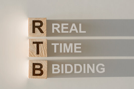 RTB - short for Real Time Bidding in wooden alphabet letters with text on shadows on light gray background.