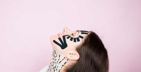 Portrait of woman with colorful tapes on face and neck on pink surface. Face aesthetic taping. Lifting skin concept