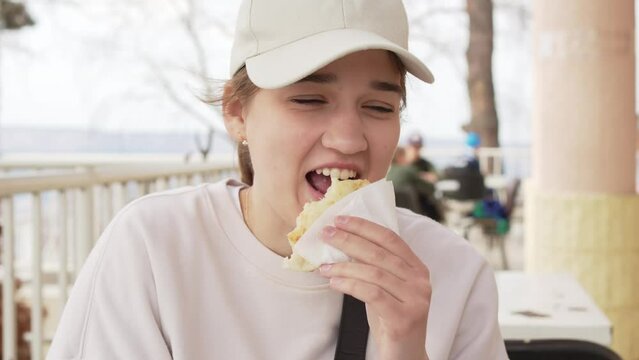 a cheerful girl in a cap eats flatbread with cheese. 