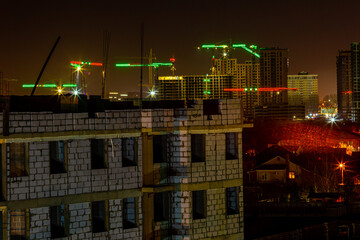 Glowing construction cranes against the background of the night sky and a house under construction