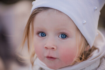 A very close-up portrait of a little blonde girl with blue eyes in a white cap. Allergy on the face