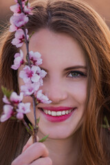Close-up portrait of millennial woman holding blooming pink sakura branch near face. Natural beauty