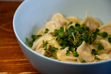 Delicious meat dumplings in the blue bowl on the wooden background. Fresh micro greens in a bowl with dumplings. Ukrainian traditional dish
