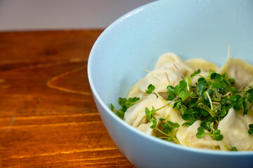 Delicious meat dumplings in the blue bowl on the wooden background. Fresh micro greens in a bowl with dumplings. Ukrainian traditional dish