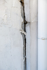 A large crack in the white concrete wall of the urban house.