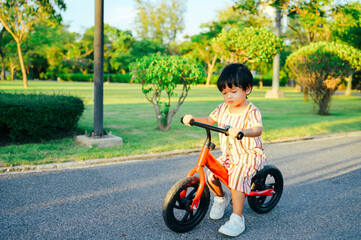 Baby boy riding  balance bike in park with soft-focus and over light in the background