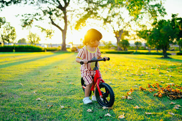 Baby boy riding  balance bike in park with soft-focus and over light in the background