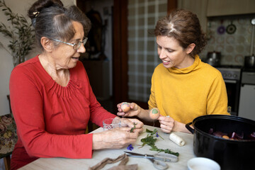 Senior Woman Learning How To Create Original Design Easter Eggs With Mid Adult Woman in Domestic Kitchen