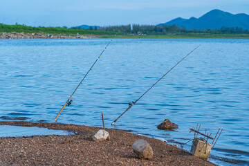 Two fishing rods set up by anglers in the lake are lowered into the water to lure the fish to bait.