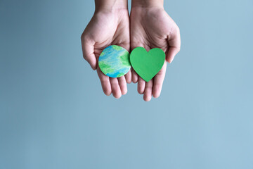 Hands holding earth and green heart shape. Concept of protecting the world from global warming with eco-heart in mind.