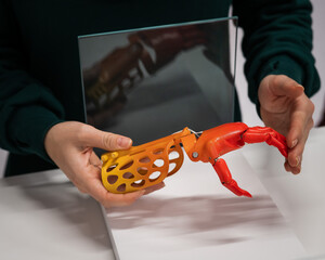 A woman demonstrates a plastic children's prosthetic hand printed on a 3D printer. 