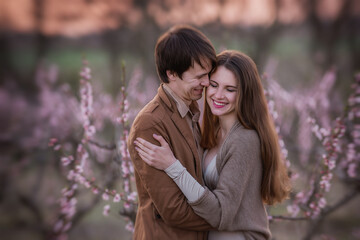 Happy couple in love at sunset in blooming peach rose gardens. Man stands in front of young woman, hugs, kisses with tenderness and passion. Romantic date, lovers honeymoon out of town on the weekend