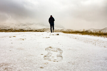 Man walks blurred ahead and his footprint is clearly visible on this side in snowy path