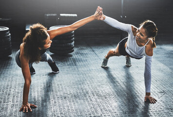Fototapeta na wymiar Bring your best friend and give it your best. Shot of two young women giving each other a high five while doing push ups at the gym.